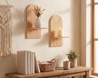 May include: Two wooden arched wall shelves with a natural finish. One shelf holds a white vase with dried flowers, the other a candle. A macrame wall hanging, books, a basket, a mug, and a potted plant sit on a wooden table.