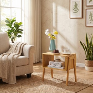 May include: A light wood side table with a rectangular top and a lower shelf. The table has four angled legs and a geometric design. A blue vase with flowers, a plate with cake, and a teacup sit on top. Books and a decorative object are on the shelf.