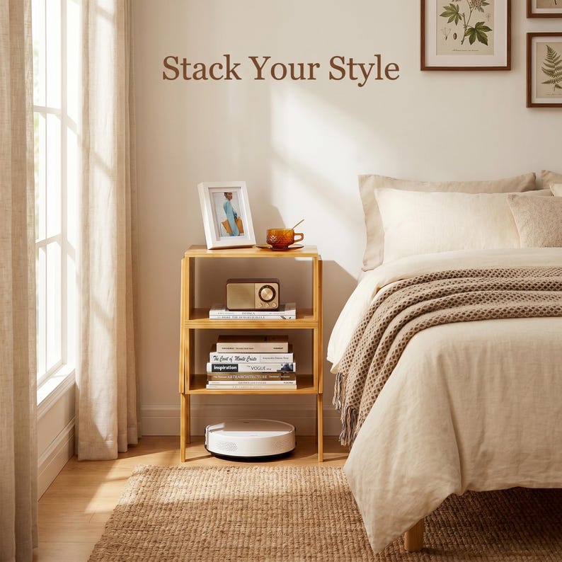 May include: A three-tiered, light-colored wooden side table with items on each shelf. A framed photo, radio, books, and a coffee cup are visible. A robotic vacuum cleaner sits on the floor. The text "Stack Your Style" is above the table.