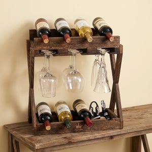 May include: A rustic wooden wine rack holds eight wine bottles and several wine glasses. The rack is stained a dark brown and has a built-in area for hanging wine glasses. A corkscrew and bottle opener are also visible.