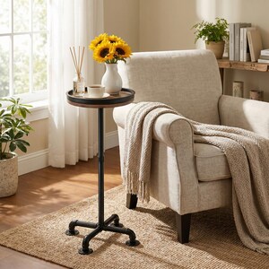 May include: A small, round side table with a black metal base and a wooden top. The table holds a vase of sunflowers, a cup of coffee, and a reed diffuser. A beige armchair and a woven rug complete the cozy living room scene.