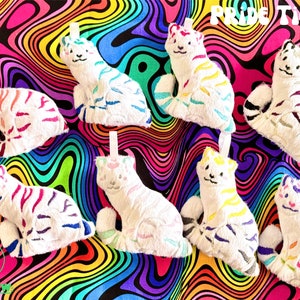 May include: Eight plush white tiger toys with rainbow stripes. The tigers are sitting on a colorful psychedelic background. The text "PRIDE TIGERS!" is at the top of the image.