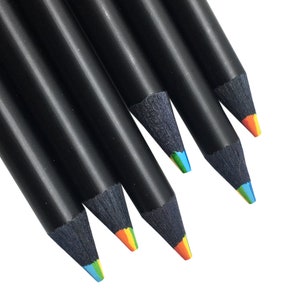 May include: A collection of five sharpened pencils with matte black wooden barrels. Each pencil features a multi-colored core that reveals a blend of vibrant pigments including blue, green, yellow, and orange at the pointed tips.