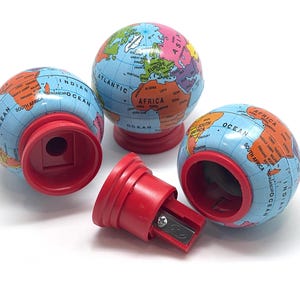 May include: A collection of globe-shaped pencil sharpeners. The globes are blue with continents in various colors and red bases. One sharpener is disassembled, showing the red body and the blade.