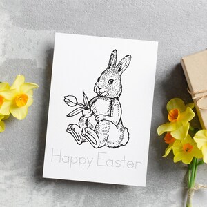 May include: A black and white illustration of a rabbit holding a tulip with the text "Happy Easter" on a white card.