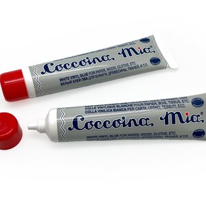 May include: Two tubes of white vinyl glue labeled "Coccoina, Mia." The glue is for paper, wood, clothes, and other materials. The tubes are silver with blue lettering and red caps.