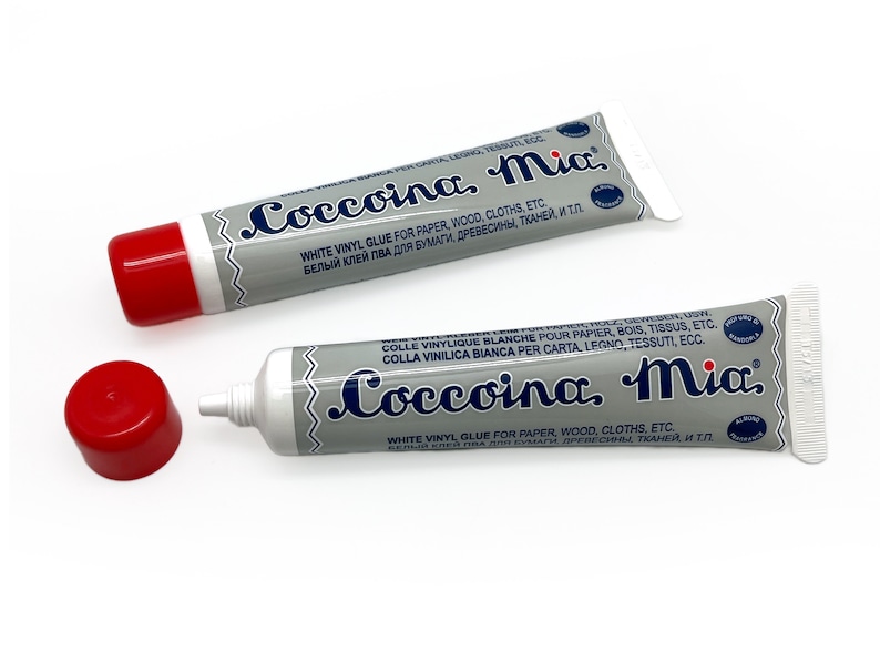 May include: Two tubes of white vinyl glue labeled "Coccoina, Mia." The glue is for paper, wood, clothes, and other materials. The tubes are silver with blue lettering and red caps.
