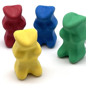 May include: Four colorful, bear-shaped game pieces in red, blue, green, and yellow. The pieces are made of a smooth material and are arranged on a white surface. These game pieces are likely for a board game.