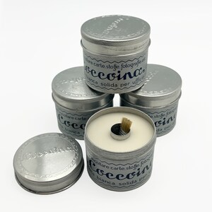 May include: A stack of four silver tins with white glue inside. The tins have a blue label with the text "incollare carte, stoffe, fotografie etc. "occoina" bianca solida per ufficio."