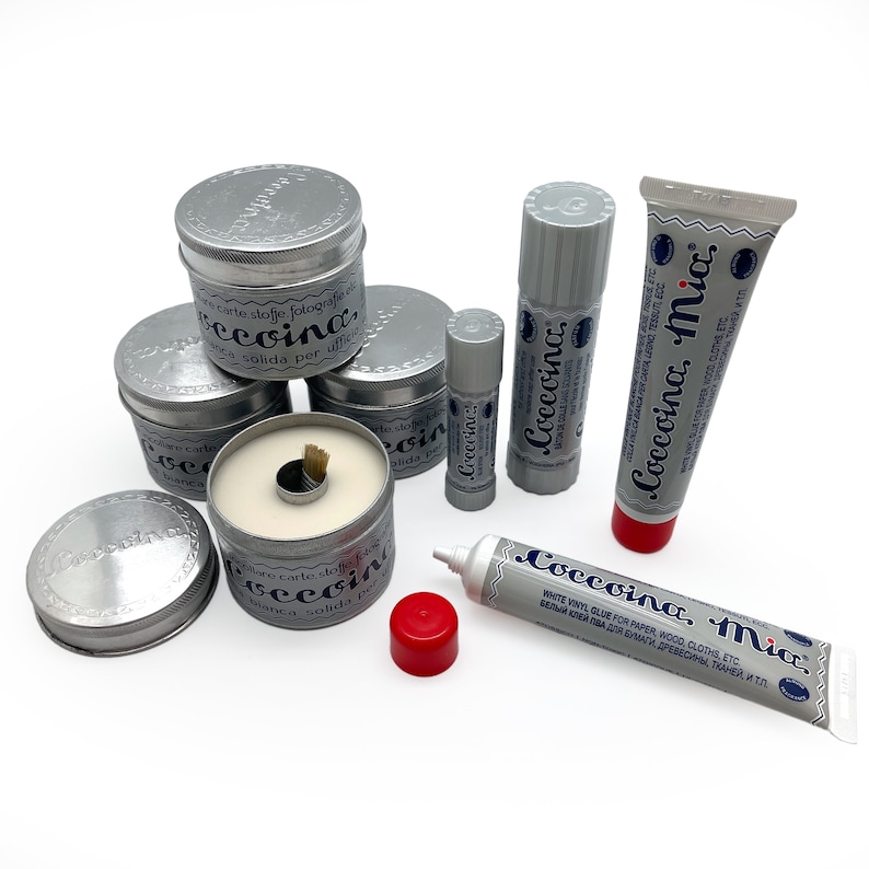 May include: Assortment of silver glue sticks and tubes labeled "Coccoina Mia" in blue and white lettering. The glue is for paper, wood, cloth, and other materials.