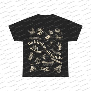 May include: Black t-shirt with cream-coloured illustrations of insects, including butterflies and beetles. The text "be kind to all kinds" is printed in a curved layout. The design features a variety of insects, such as a snail and a dragonfly.