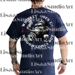 Op de afbeelding: Marineblauw t-shirt met een afbeelding van een gorilla die een sigaar rookt en een glas whisky. De tekst luidt "Whiskey Goes In, Wisdom Comes Out" in een cirkelvormig ontwerp. Een rode bliksem is ook zichtbaar.