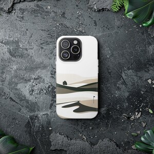May include: A white phone case with a landscape design featuring a small tree, hills, and a golf flag. The case has a black camera bump with three lenses.