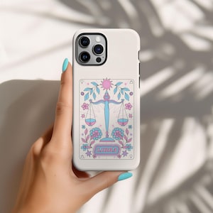 May include: White phone case with a pink and blue Libra zodiac sign illustration. The illustration features a scale, flowers, and the word "Libra".