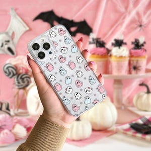 Puede incluir: Una funda transparente para teléfono con un patrón de fantasmas rosas y azules con flores sobre un fondo blanco.