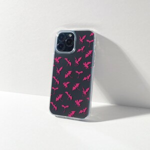 May include: A clear phone case featuring a black background adorned with a pattern of pink dragon silhouettes. The case has a transparent border and covers the phone's back and sides, with cutouts for the camera and buttons.