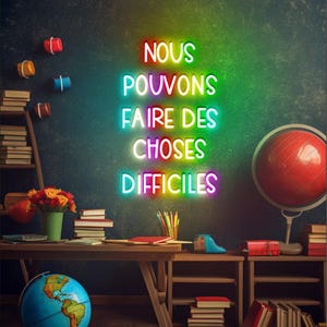 May include: A classroom scene with a neon sign that reads "NOUS POUVONS FAIRE DES CHOSES DIFFICILES". The sign is in rainbow colors and is mounted on a dark green chalkboard. There are books, pencils, and a globe on a wooden desk in the foreground.
