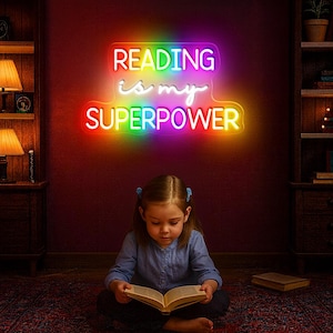 Può includere: Un'insegna al neon colorata con la scritta "READING is my SUPERPOWER" è appesa sopra una bambina che legge un libro. L'insegna ha un gradiente arcobaleno ed è montata su una parete rosso scuro. La bambina indossa una camicia blu.
