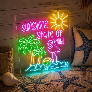 May include: A neon sign displaying the words "sunshine state of mind" in pink, with a yellow sun, green palm trees, and a pink flamingo. The sign is on a clear acrylic panel, ideal for coastal decor.