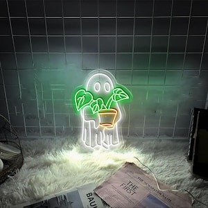 Könnte beinhalten: Ein weißes Neon-Schild in Form eines Geistes, der eine grüne Topfpflanze hält. Das Schild leuchtet in einem warmen Weiß.