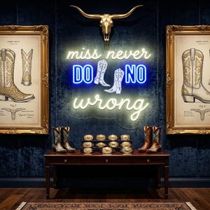 Puede incluir: Una exhibición con botas de vaquero, hebillas de cinturón e ilustraciones enmarcadas. Un letrero de neón dice "miss never do no wrong". Una calavera de toro dorada cuelga arriba. Las botas son marrones y turquesas, y las hebillas son doradas.