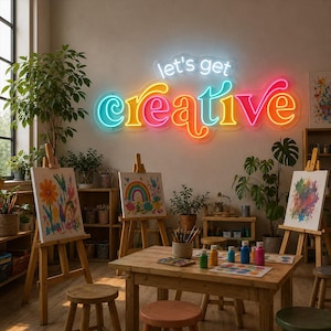 Puede incluir: Un letrero de neón en la pared muestra el texto let's get creative en letras brillantes de color azul, amarillo, naranja y rosa. La habitación cuenta con tres caballetes de madera con pinturas coloridas, una mesa de madera y plantas.