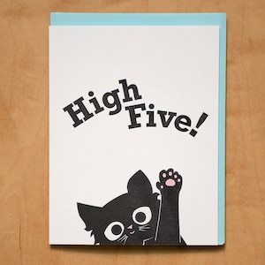 May include: A greeting card with a black cat giving a high five. The card says "High Five!" in black text.