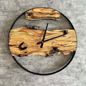 Könnte beinhalten: Eine runde Wanduhr mit schwarzem Metallrahmen und einem natürlichen Holzgesicht. Das Holz hat eine einzigartige Maserung und eine natürliche Kante. Die Uhrzeiger sind schwarz.