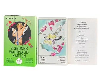 May include: A vintage set of fortune telling cards with a green background and a cupid illustration. The cards are labelled "Zigeuner Wahrsage-Karten" in German, which translates to "Gypsy Fortune Telling Cards". The cards are printed in multiple languages, including German, English, Hungarian, Italian, Croatian, and French.