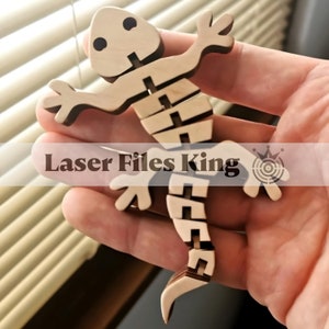 May include: A wooden articulated lizard toy with a light brown body and dark brown accents. The lizard is made of interlocking pieces and has the text "Laser Files King" on the image.