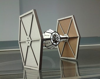 May include: A white and brown wooden model of a TIE fighter from the Star Wars franchise. The model is made of laser-cut wood and has a detailed design.