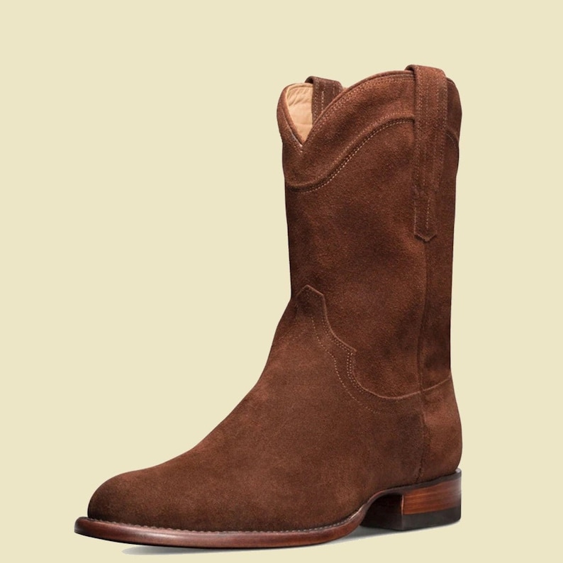 May include: Brown suede cowboy boots with a pointed toe and a low heel.