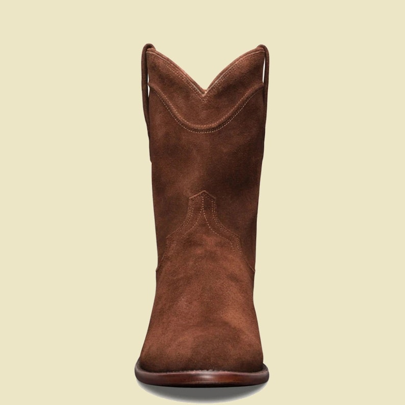 May include: Brown suede cowboy boots with a pointed toe and a low heel.