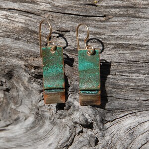 May include: A pair of earrings with a green and copper finish. The earrings are rectangular in shape and have a gold hook.