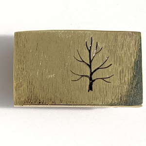 May include: A gold-colored metal rectangle with a tree silhouette cut out in the center.