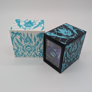 May include: Two rectangular card storage boxes, one white with cyan graphics and one black with cyan graphics. The black box features a clear front window displaying a single trading card with purple artwork and the text "Glimmer" visible.