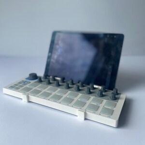 May include: White electronic music production pad with gray knobs and a tablet computer on top.