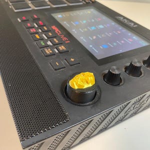 May include: Black Akai MPC Live II music production sampler with a gold knob and a screen displaying the word "MPC Live II".