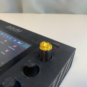 May include: A close-up of a gold knob on a black music production device. The knob is labelled "Q-LINK".