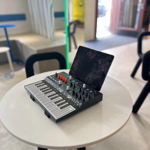 May include: A black and white keyboard with orange buttons and a black and white tablet on top of it. The keyboard is sitting on a white table.