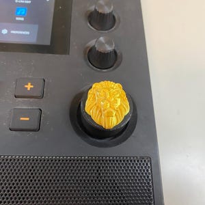 May include: A gold lion head knob for a music production controller. The knob is made of plastic and has a detailed design.