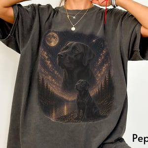 Puede incluir: Camiseta gris oscuro con un dise&ntilde;o de un Labrador Retriever negro sobre un fondo de luna llena y cielo estrellado. El dise&ntilde;o incluye dos im&aacute;genes del perro. La palabra "Pepper" est&aacute; impresa en la camiseta. La camiseta es de corte holgado.