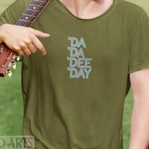 May include: A green t-shirt with the text "DA DA DEE DAY" printed in a light blue color.