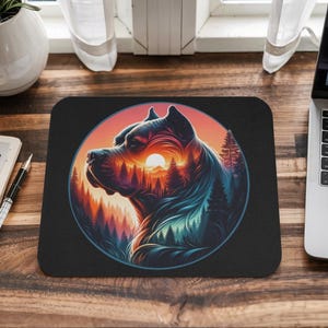 May include: A black mousepad with a circular design featuring a silhouette of a dog's head with a forest scene inside. The dog's eye is a sunset with a mountain range in the background.