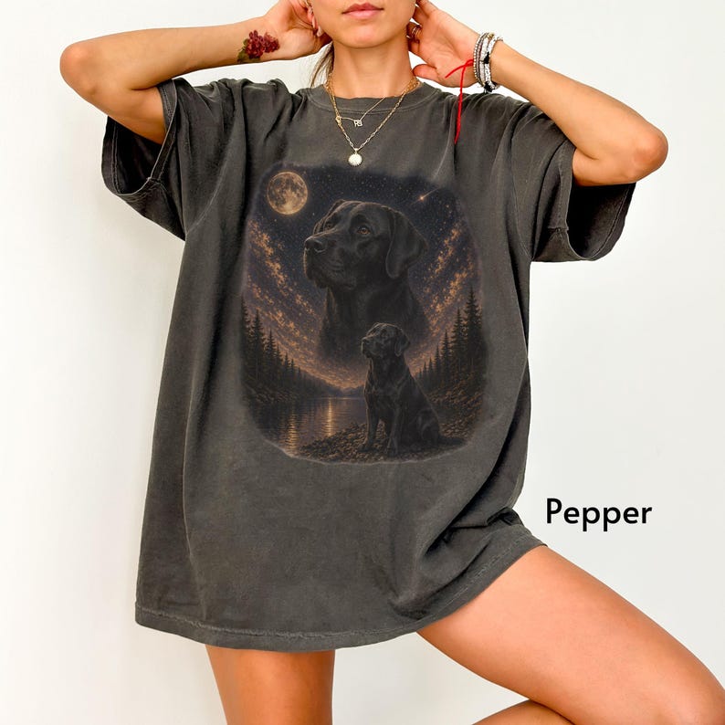 Puede incluir: Camiseta gris oscuro con un dise&ntilde;o de un Labrador Retriever negro sobre un fondo de luna llena y cielo estrellado. El dise&ntilde;o incluye dos im&aacute;genes del perro. La palabra "Pepper" est&aacute; impresa en la camiseta. La camiseta es de corte holgado.