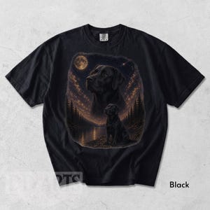 Puede incluir: Camiseta negra con una ilustraci&oacute;n detallada de un Labrador Retriever negro bajo un cielo estrellado con luna llena. El dise&ntilde;o incluye un retrato m&aacute;s grande y una imagen m&aacute;s peque&ntilde;a del perro cerca de un lago y &aacute;rboles.