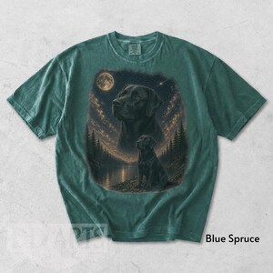 Puede incluir: Camiseta azul abeto con un gr&aacute;fico de un Labrador Retriever negro bajo un cielo estrellado y una luna llena. El dise&ntilde;o incluye una silueta de perro junto a un lago y &aacute;rboles. La camiseta tiene un corte holgado.