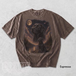Puede incluir: Camiseta color espresso con una ilustraci&oacute;n detallada de un Labrador Retriever negro bajo un cielo estrellado con luna llena. El dise&ntilde;o incluye un retrato m&aacute;s grande y una imagen m&aacute;s peque&ntilde;a del perro cerca de un lago y &aacute;rboles.