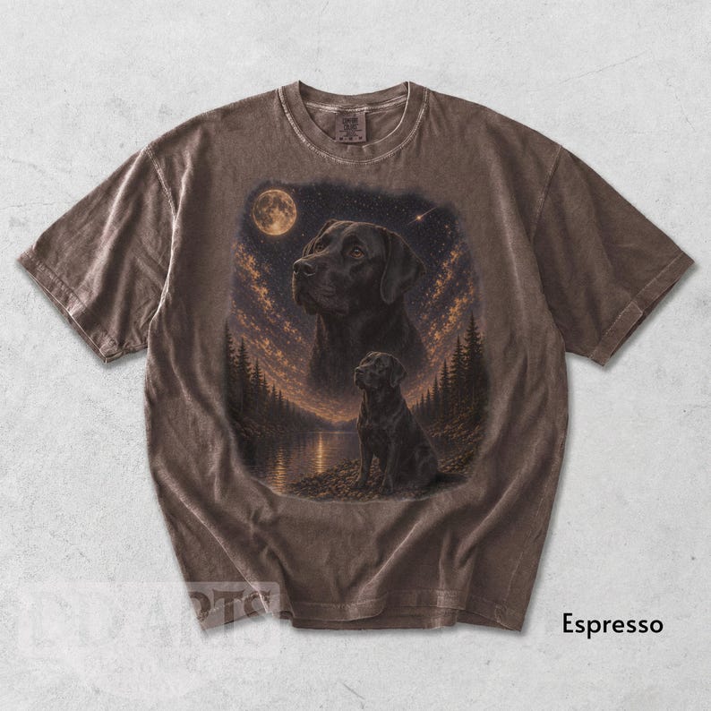 Puede incluir: Camiseta color espresso con una ilustraci&oacute;n detallada de un Labrador Retriever negro bajo un cielo estrellado con luna llena. El dise&ntilde;o incluye un retrato m&aacute;s grande y una imagen m&aacute;s peque&ntilde;a del perro cerca de un lago y &aacute;rboles.