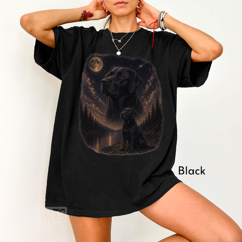 Puede incluir: Camiseta negra con un gr&aacute;fico de un Labrador Retriever negro bajo una luna llena y un cielo estrellado. El dise&ntilde;o incluye un lago y una escena de bosque. La palabra "Black" est&aacute; impresa en la parte inferior derecha.